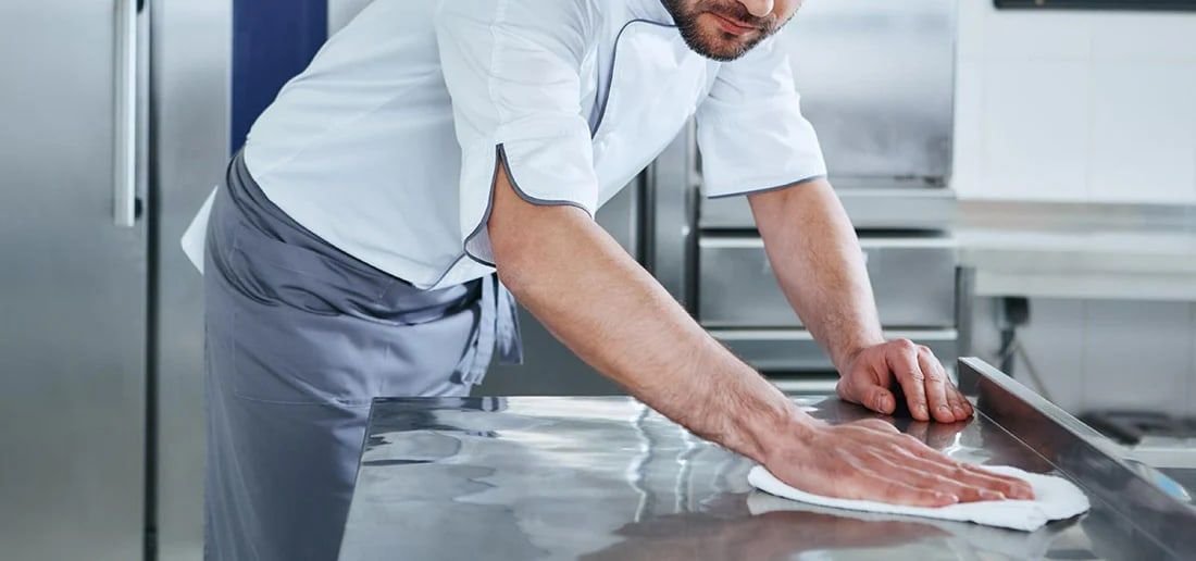 Persona limpiando el mesón de acero de una cocina