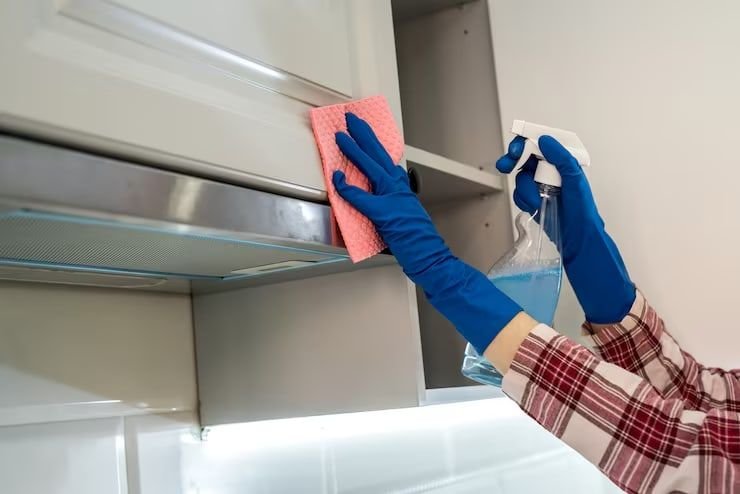 Manos con guantes limpiando un estante de cocina
