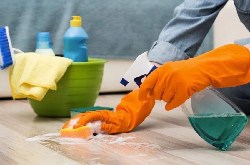 Manos con guantes limpiando una superficie con productos de aseo