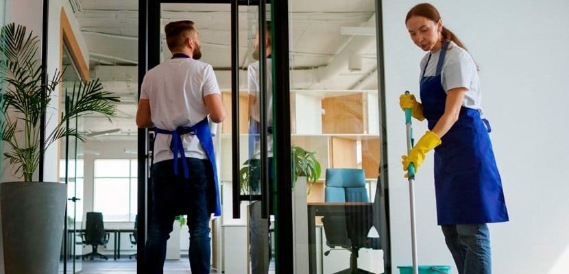 Dos personas del equipo de aseo limpiando una oficina